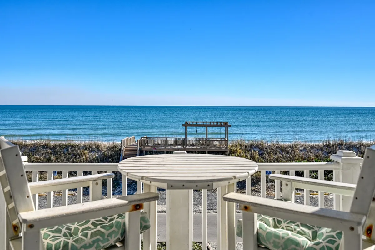A breathtaking beachfront view with comfortable outdoor seating overlooking calm ocean waters. The expansive horizon and tranquil sea set the stage for relaxation and outdoor gatherings, hinting at the easy access to beach activities right outside your door.