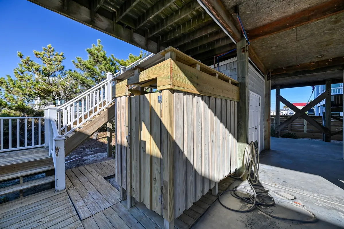 This image features an outdoor shower beside wooden stairs, surrounded by greenery. The setting is casual and relaxed, ideal for rinsing off after a day at the beach—whether it's sandy feet or paws. The view highlights the shower's accessibility and its connection to the outdoor environment.