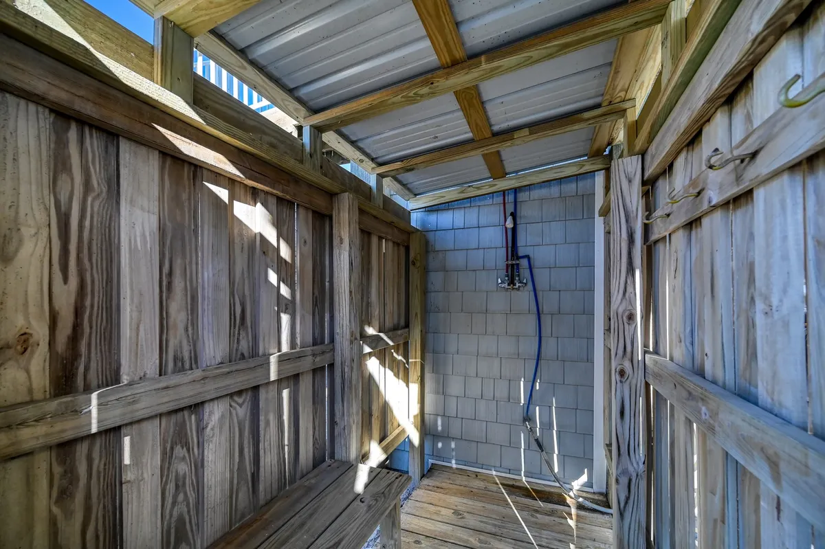 An inviting outdoor shower with wooden walls and an open ceiling sits surrounded by natural light, perfect for rinsing off after a sandy beach adventure. The rustic yet functional setup creates an atmosphere of relaxed beach living.