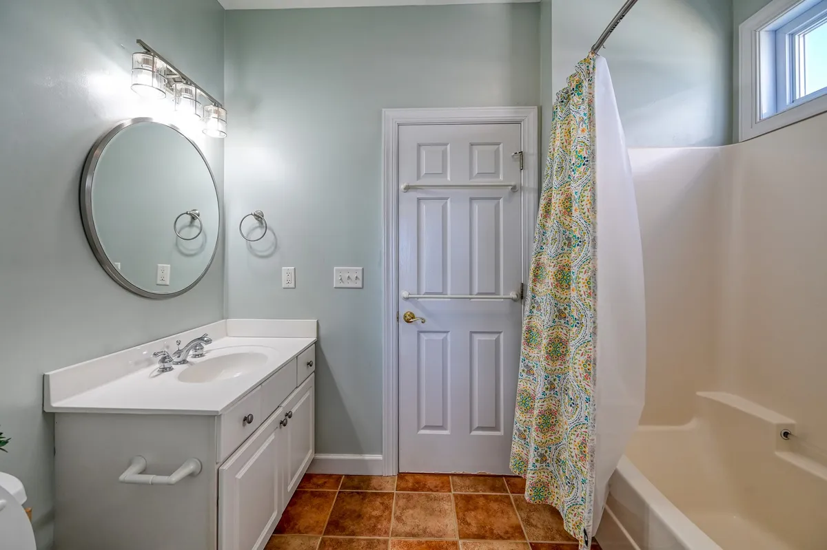 A clean and tranquil bathroom with a vanity and sink, round mirror, bathtub, and a shower curtain. Soft lighting and neutral tones evoke a sense of comfort and privacy.