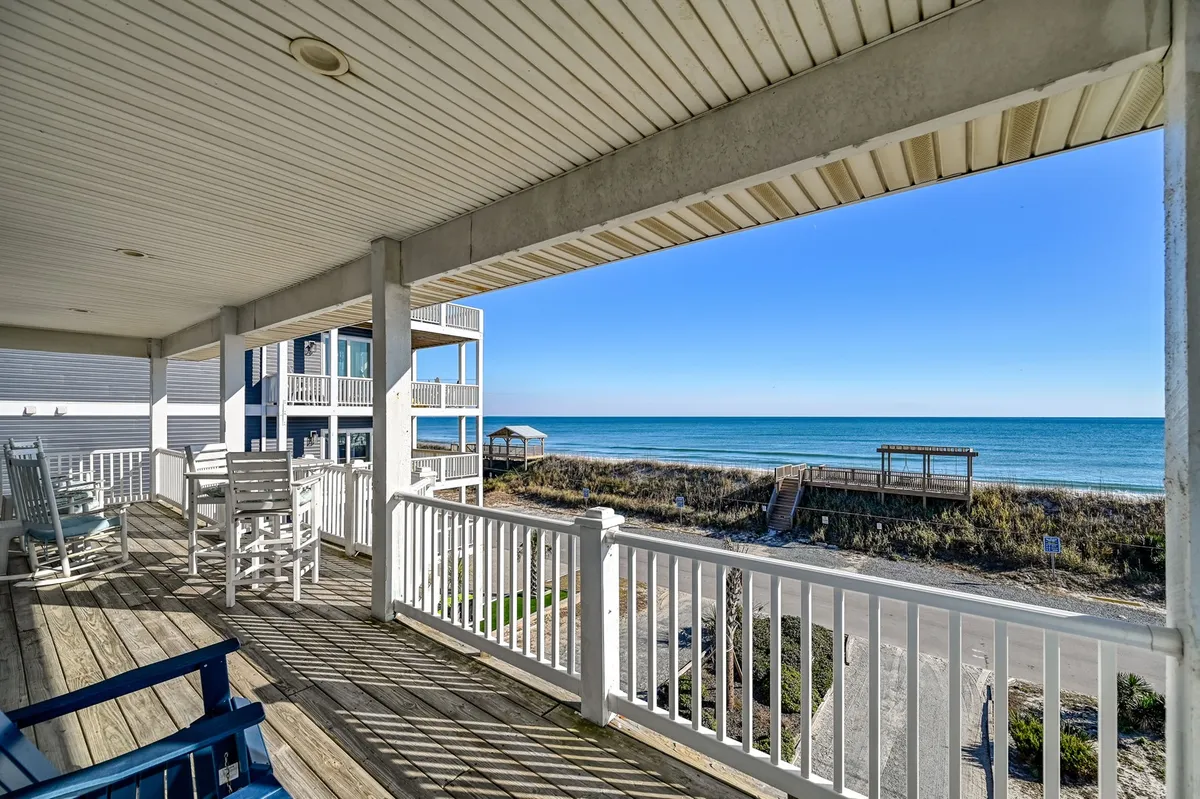 A tranquil exterior deck with porch chairs overlooks a stunning ocean view. The deck is bordered by a classic railing, creating an ideal spot for relaxing, reading, or spending quality time with your dog while taking in the sights and sounds of the sea.