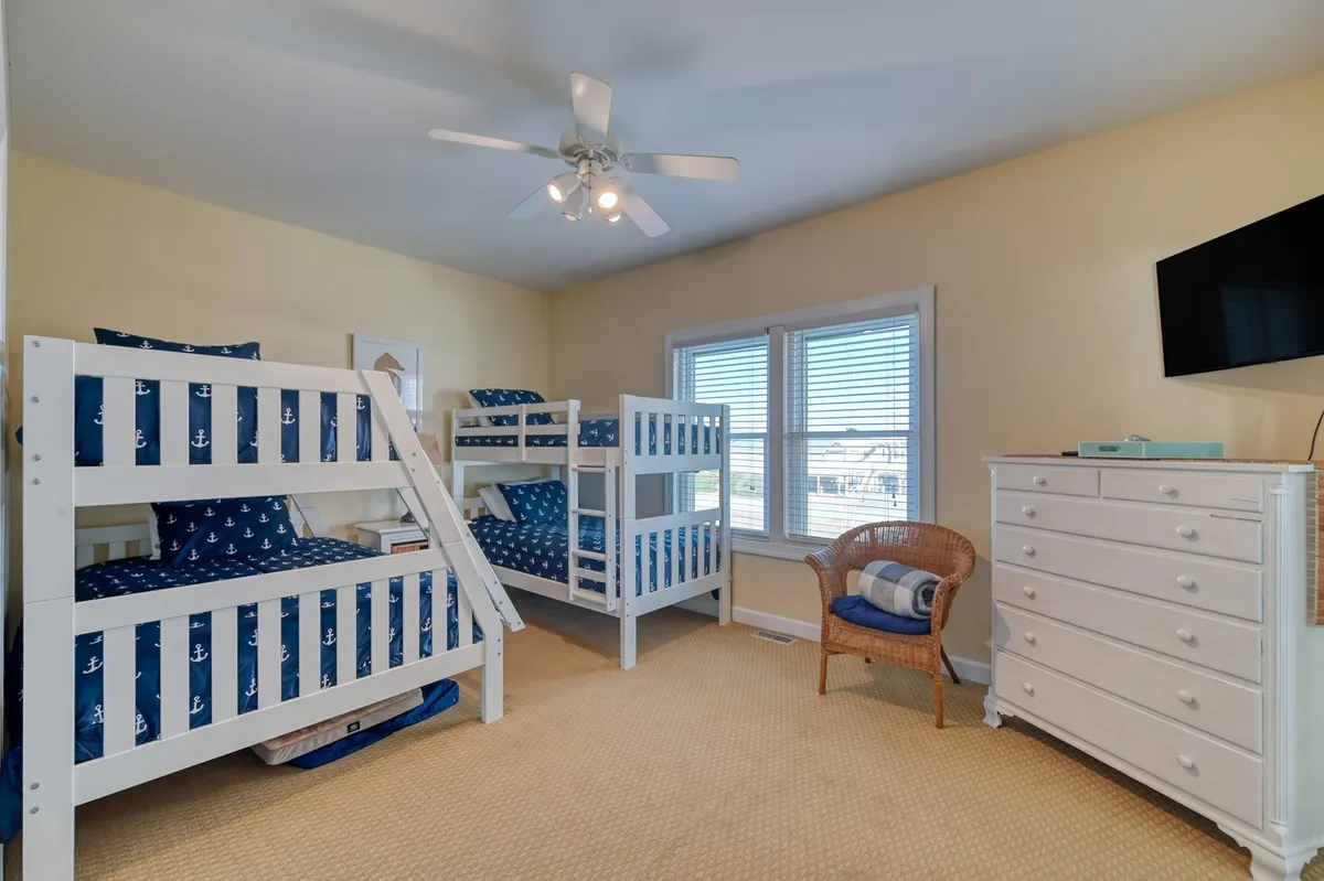 A cheerful, kid-friendly room with sturdy bunk beds, a dresser, a window with blinds, and a ceiling fan. The playful bedding and accessible storage make this space perfect for children to sleep, read, and play.