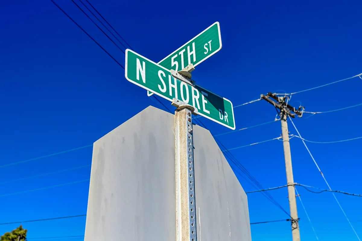 This image features a welcoming street sign set against a clear blue sky and a utility pole, evoking the inviting atmosphere of a small coastal community. The scene suggests the start of an exploration, with the sign hinting at nearby local destinations and the open sky providing a sense of space and opportunity.