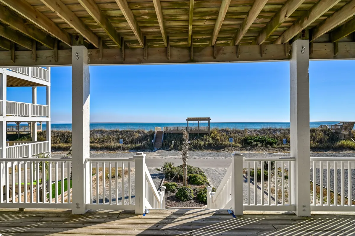 An oceanfront covered deck with deck railing, palm tree, and stairs leading to the beach. The scene offers panoramic ocean views and evokes the comfort of outdoor living, ideal for relaxing with a coffee or unwinding after a day at the beach.