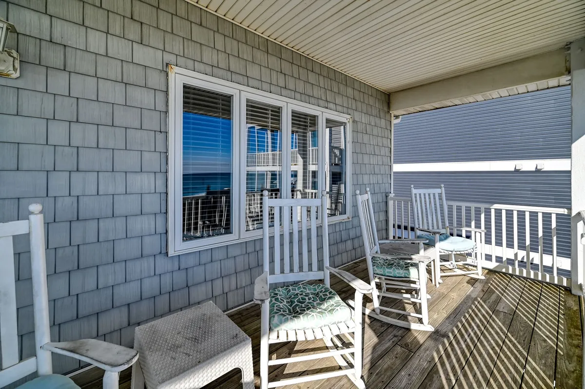 Rocking chairs line a porch with a panoramic ocean view reflected in the window, inviting guests to unwind after a day of adventure. The tranquil setting hints at leisurely mornings or sunset relaxation, perfectly complementing the theme of returning home after exploring the water.