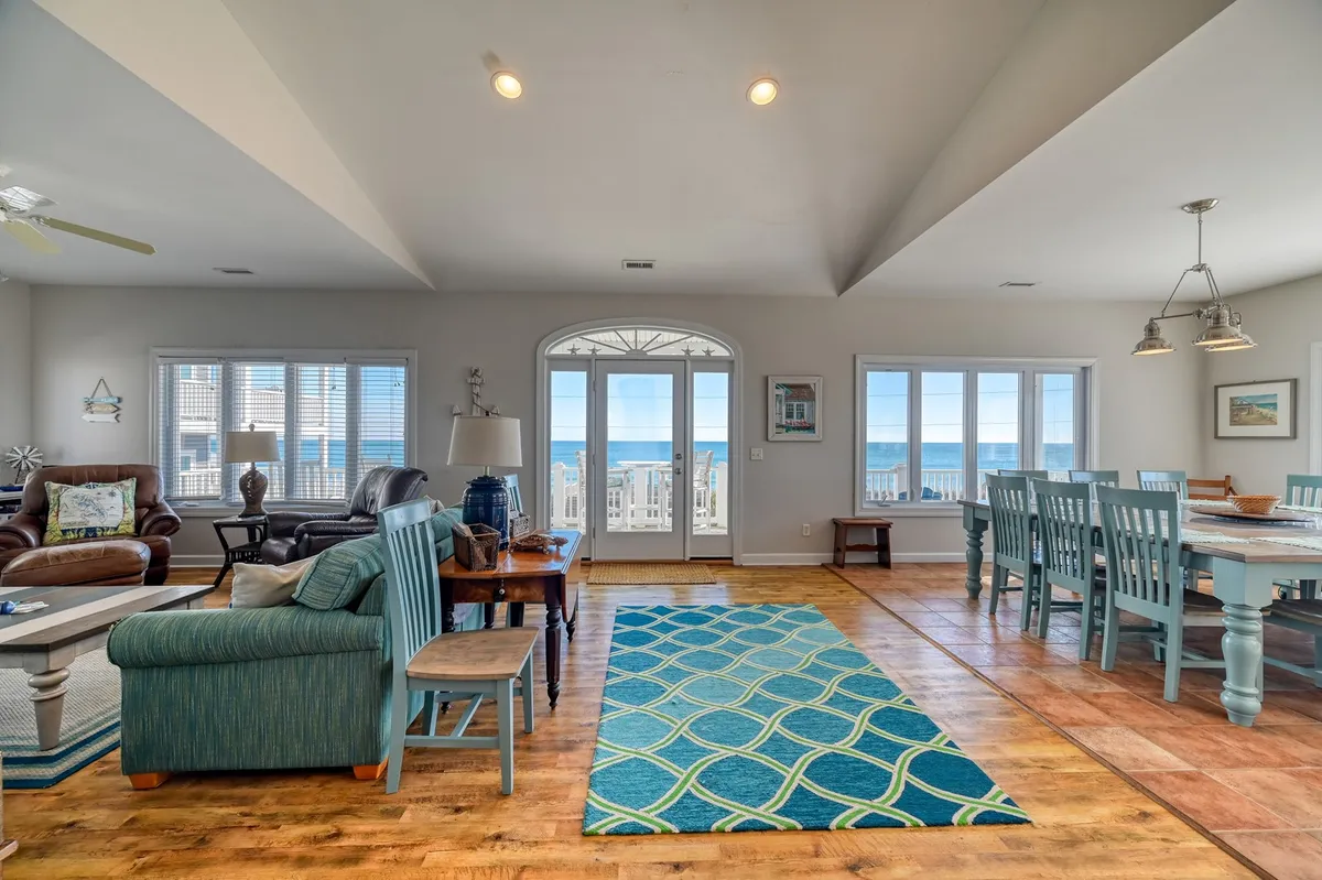 A bright, cheerful interior with large windows framing a stunning ocean view. A spacious dining table sits at the center, surrounded by comfortable seating and colorful décor, creating the perfect environment for family meals and group activities after a fun day at the beach.