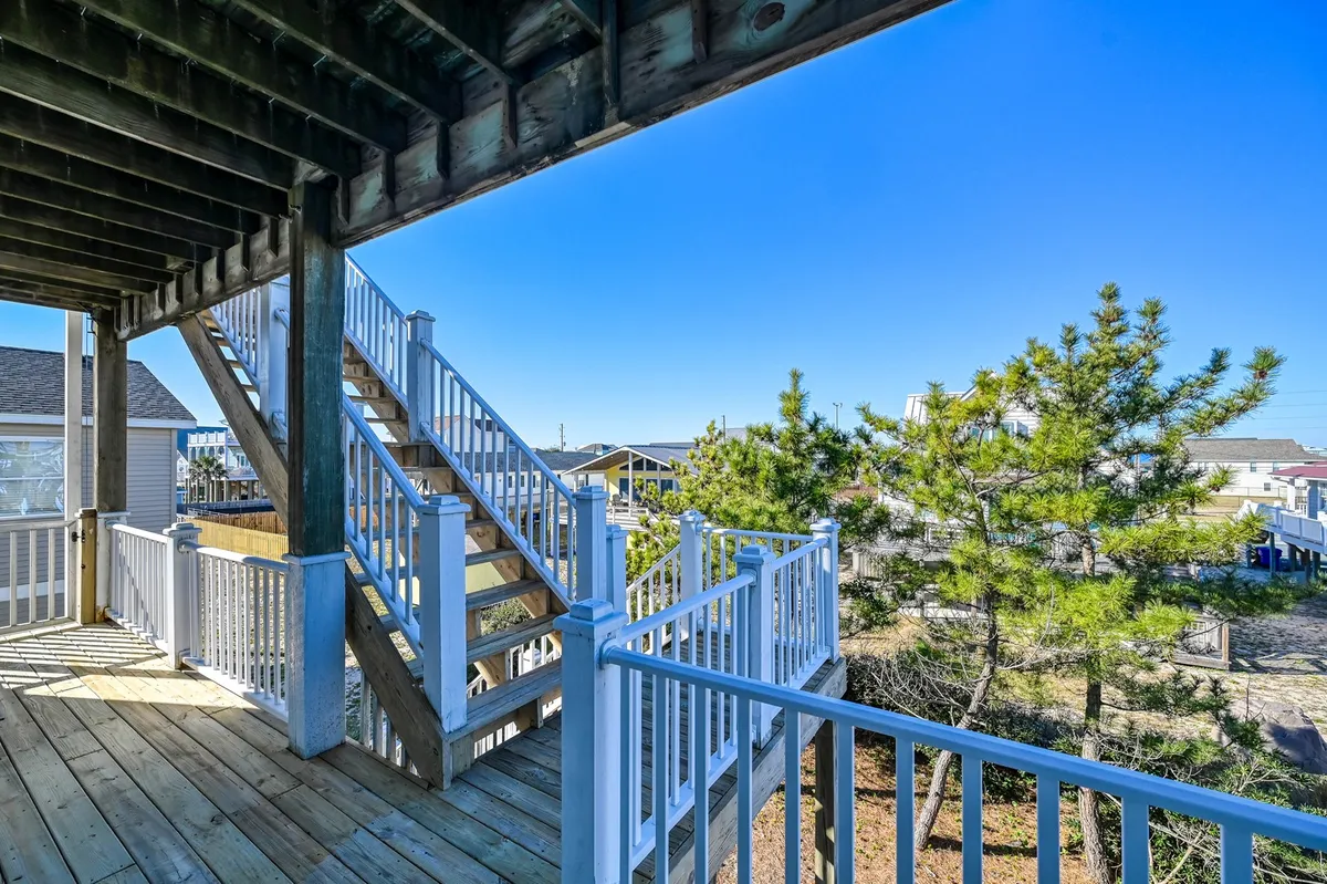A breezy exterior staircase and railings are surrounded by lush trees, offering a glimpse of elevated decks ideal for gathering, socializing, or enjoying the view. The space feels open, cheerful, and designed for both privacy and connection.