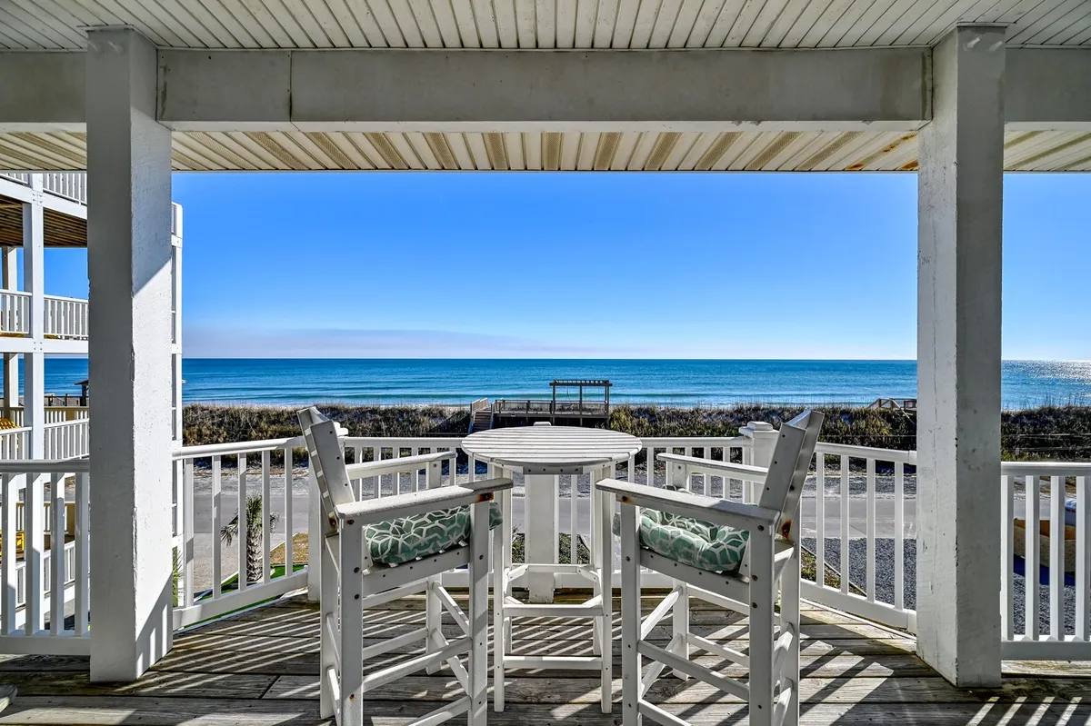 The image showcases a spacious oceanfront deck with comfortable outdoor seating, all set against a stunning backdrop of the Atlantic Ocean under clear blue skies. The inviting setup suggests a perfect spot for relaxing, sharing meals, and enjoying panoramic ocean views, with the promise of spectacular sunrises and starlit evenings.